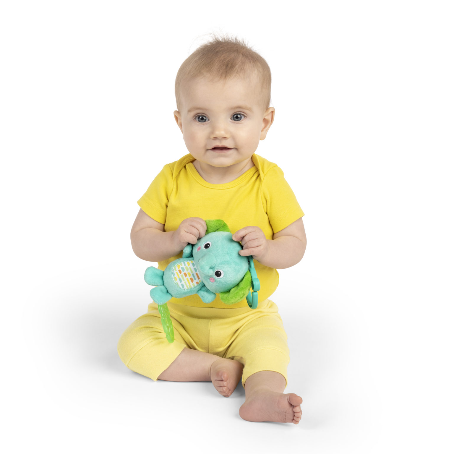 Baby holder en lyseblå og grønn leke med mønstret mage, kledd i gul body og gule bukser.