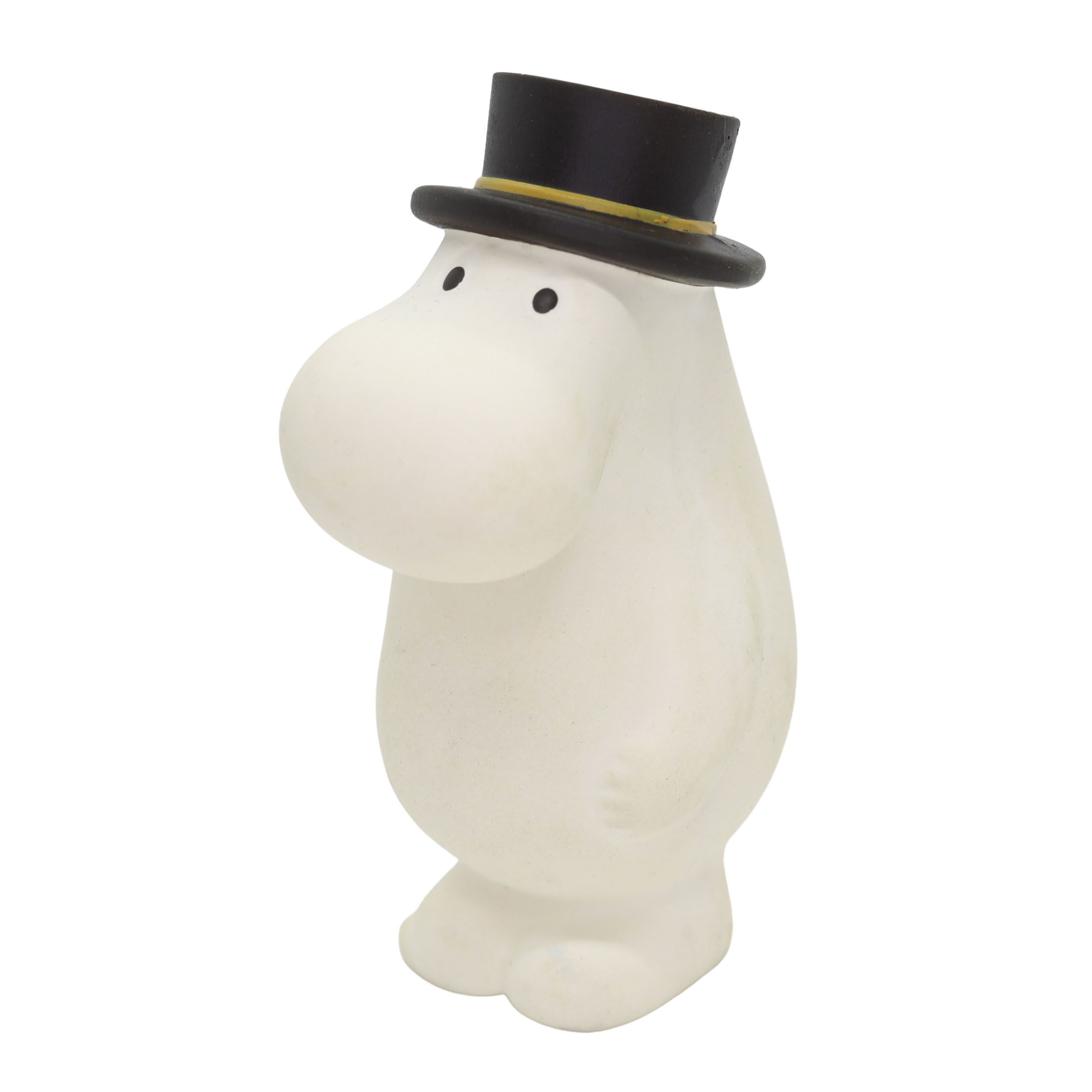 Hvit Mummifigur med svart flosshatt og gult bånd, sett fra siden.